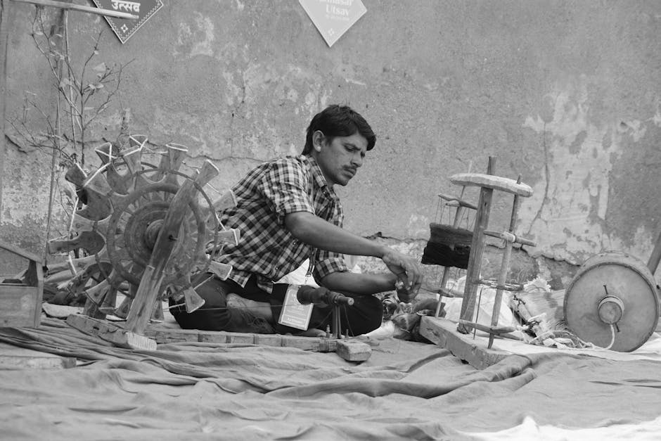 A focused Indian man operates a manual weaving machine outdoors, showcasing traditional textile craft.