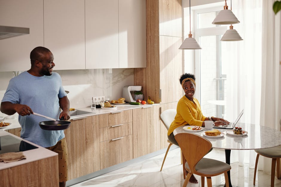 A couple enjoys their morning routine in a bright, modern kitchen, cooking and smiling.