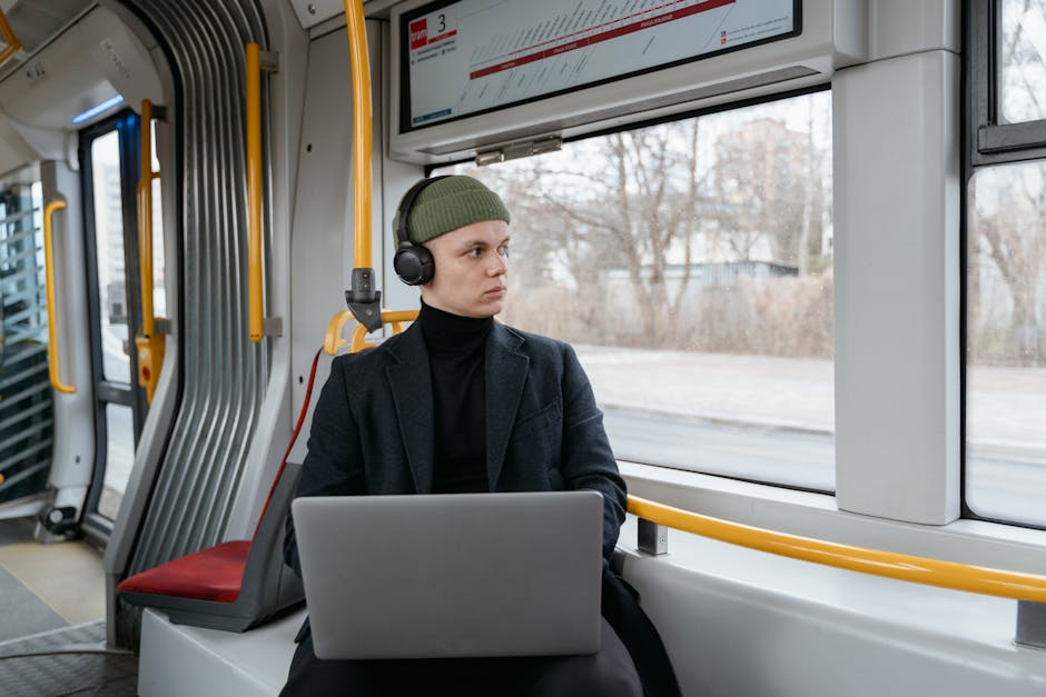 Young adult wearing headphones, using a laptop on a train. Focused and in transit.