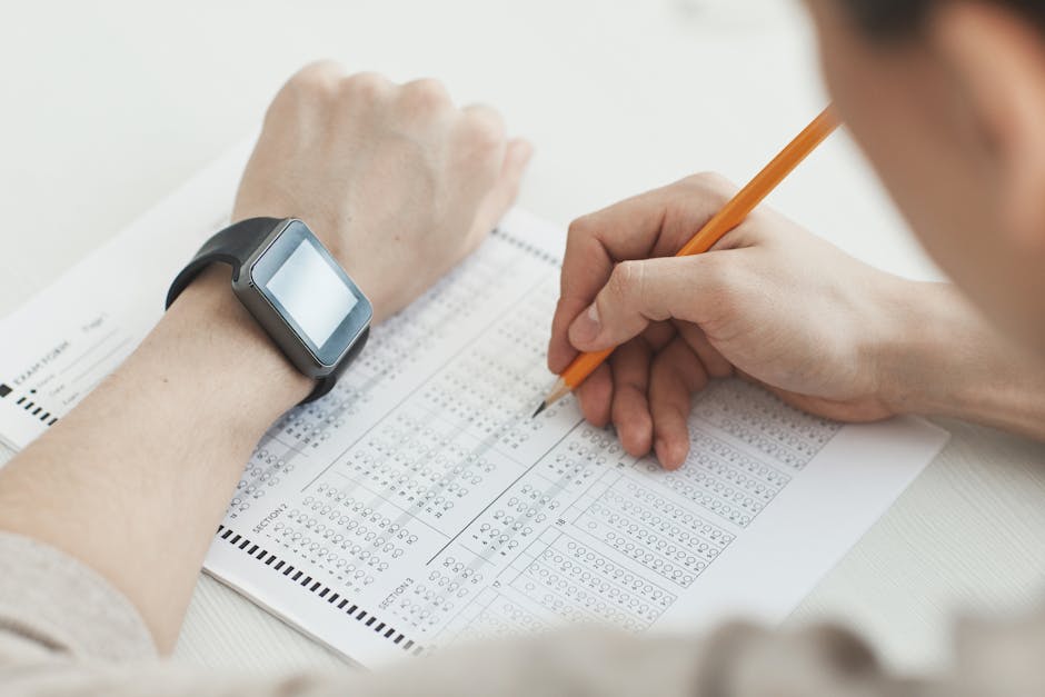 Close-up of a student writing answers on a test sheet with a pencil and smartwatch.