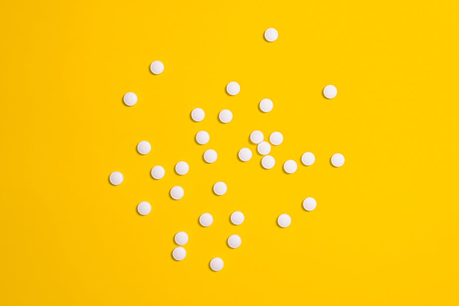White pills scattered on a vibrant yellow background, symbolizing medical treatment and health care.