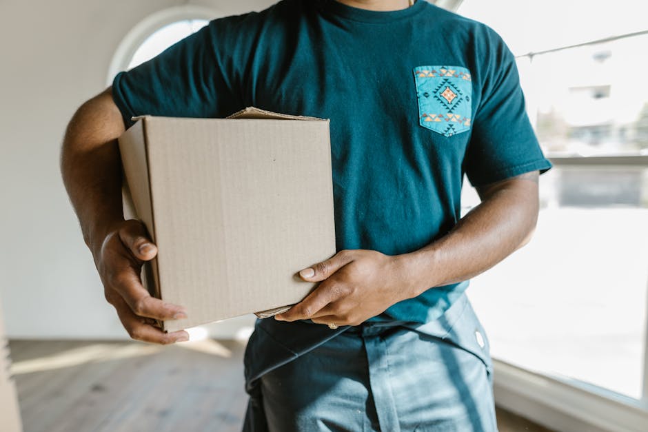 Close-up of a man holding a cardboard box in a bright room, symbolizing moving or delivery.