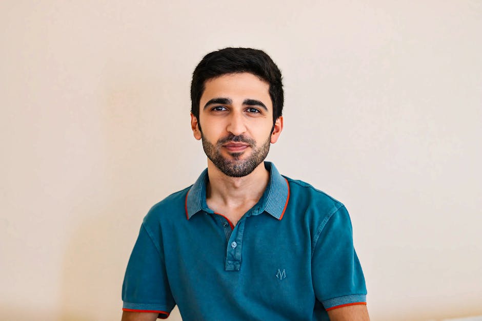Portrait of a bearded man in a teal shirt against a neutral background. Suitable for lifestyle and fashion contexts.