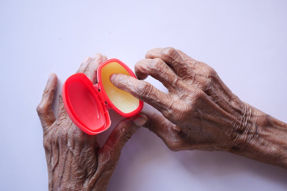 Close-up of senior hands using hand cream for skincare in a red container on a white background.