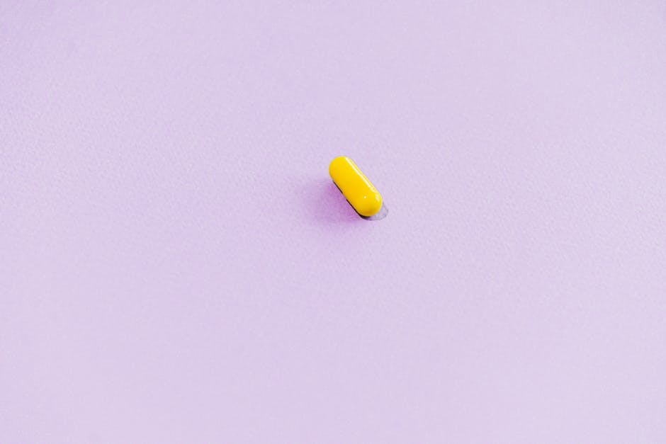 Single yellow capsule on a soft pink background, ideal for pharmaceutical themes.