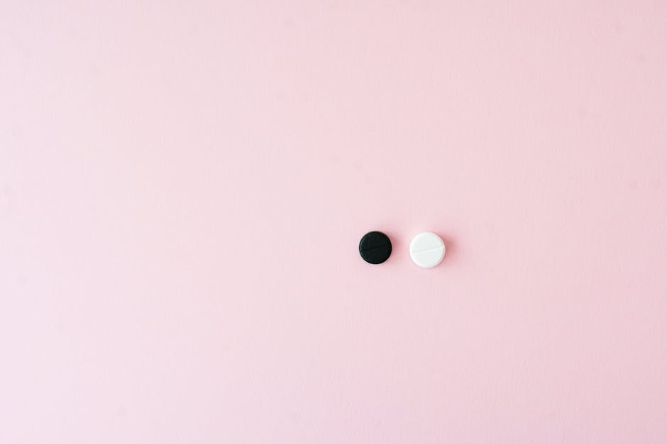 Minimalist photo of black and white pills on a pink surface, evoking contrast and simplicity.