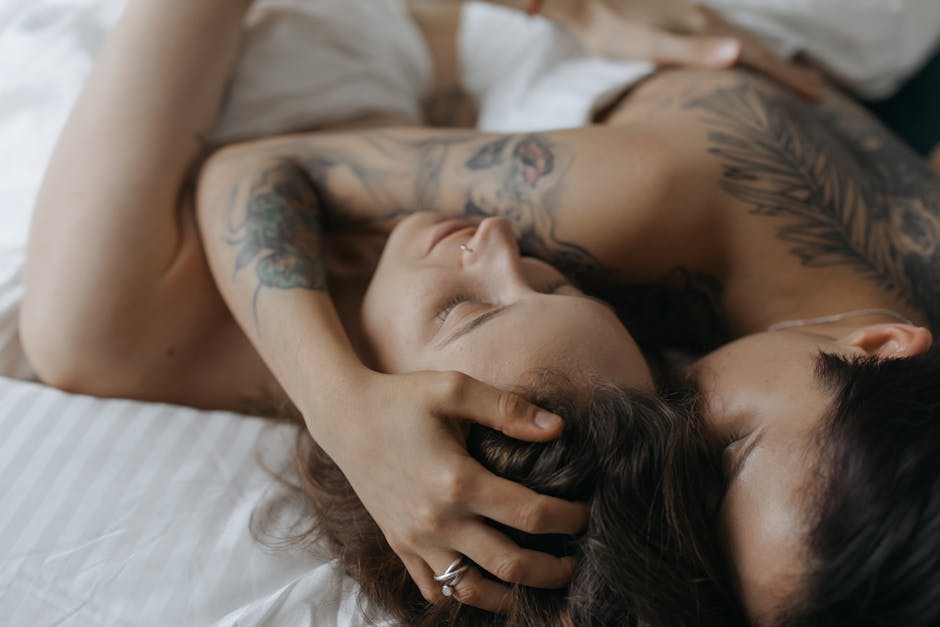 Close-up of a loving couple embracing in an intimate moment on a bed, showcasing tattoos and affection.