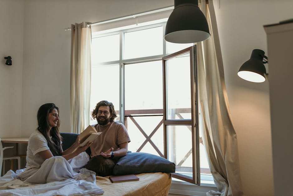 A cheerful couple laughing and sharing a book in a cozy bedroom setting.