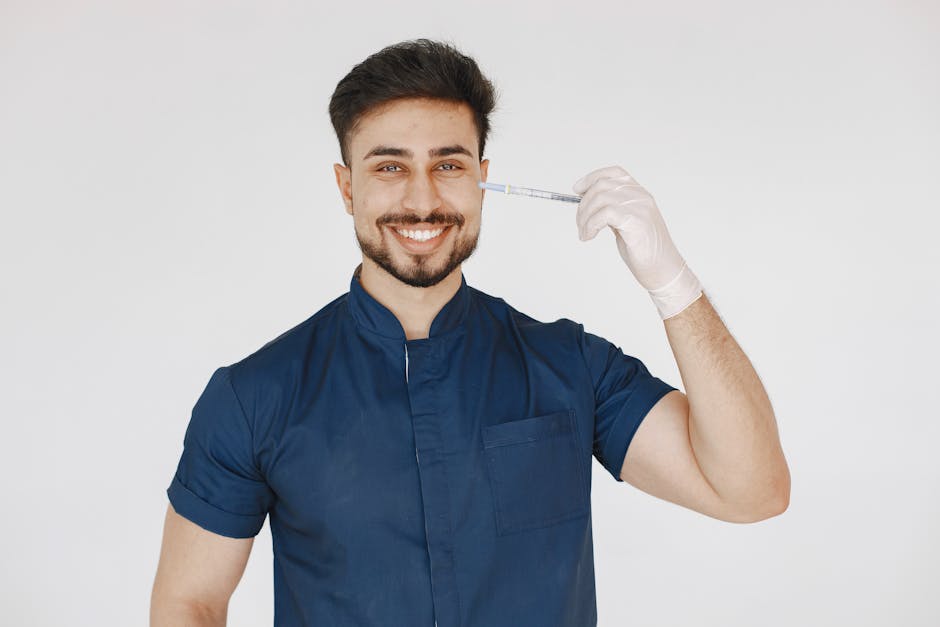 A confident doctor in blue scrubs smiling and holding a syringe in a studio setting.