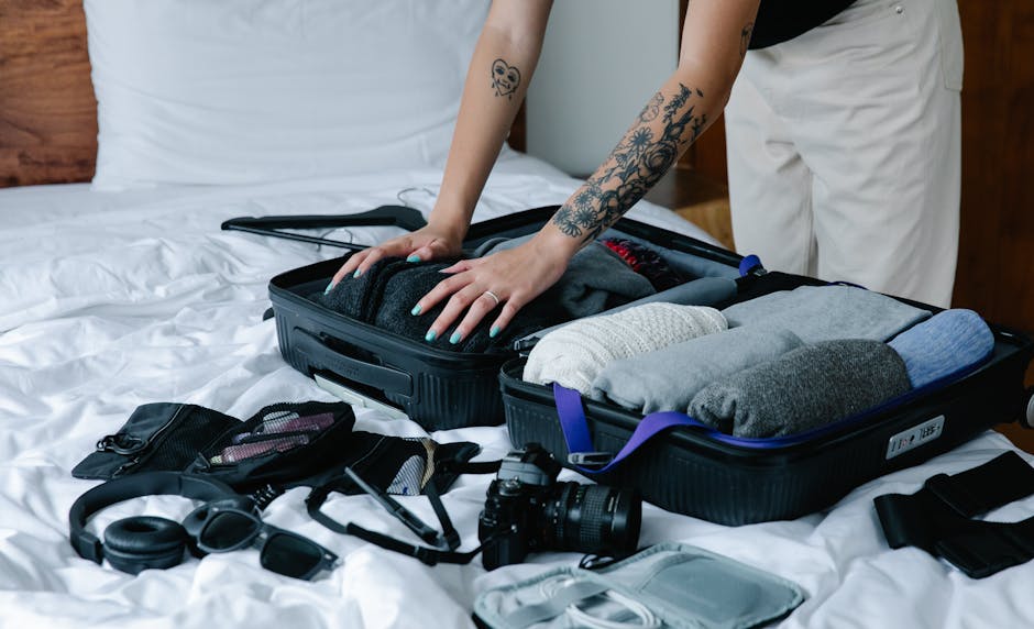 A woman with tattoos packing a suitcase on a bed, preparing for travel.