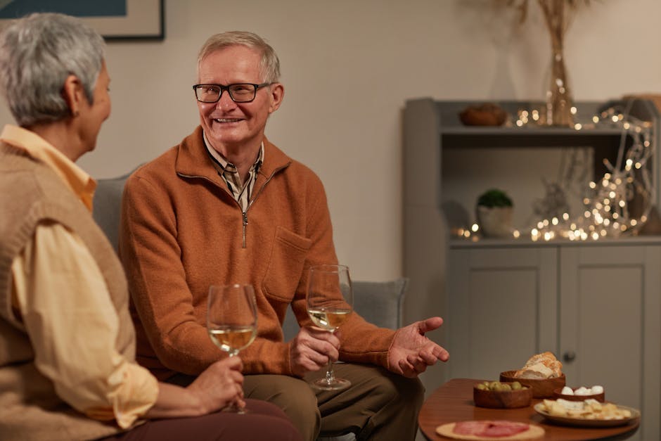 Elderly couple sharing wine and snacks in a cozy living room setting.
