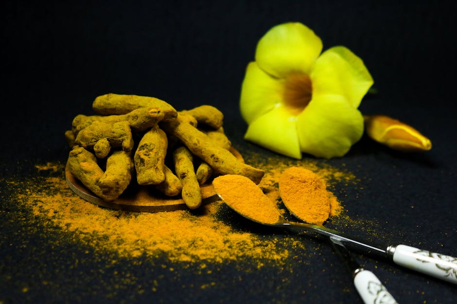 Vivid close-up of turmeric roots and powder with decorative flower on black backdrop, highlighting spice details.