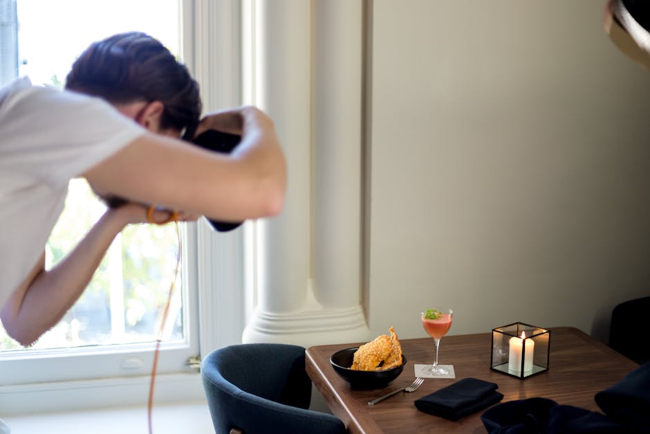 A photographer taking pictures of a stylish table with food and drinks by the window.