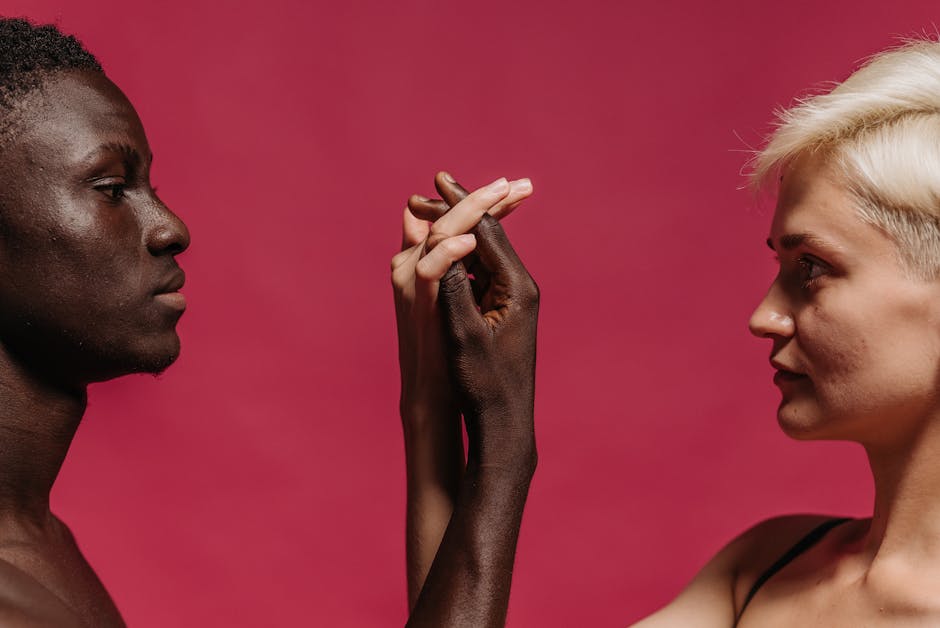 A close-up of an interracial couple holding hands against a pink background, symbolizing unity.